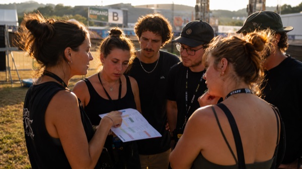 Junge Eventkoordinatorin erklärt Gruppe von Helfern den Ablauf vor einem Schweizer Openair