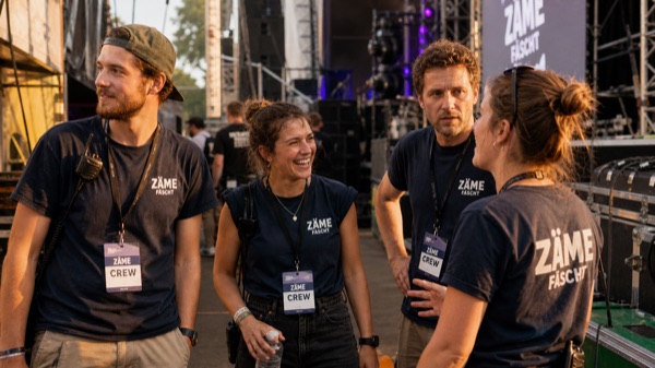 Lächelnde Helfer im Crew-Shirt vor Bühnenkulisse eines Schweizer Festivals